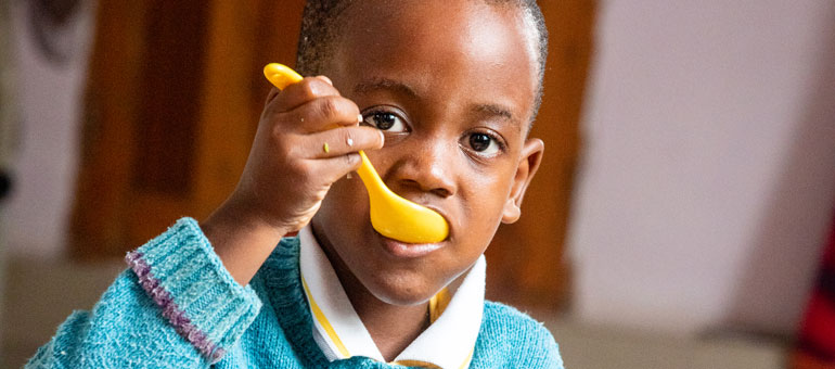 A child eating with a yellow spoon and wearing a blue sweater