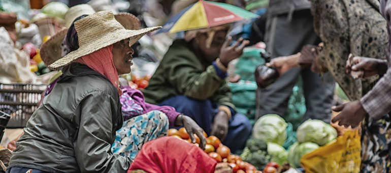 Woman wearing a hat and jacket sitting on the ground in a market in Ethiopia