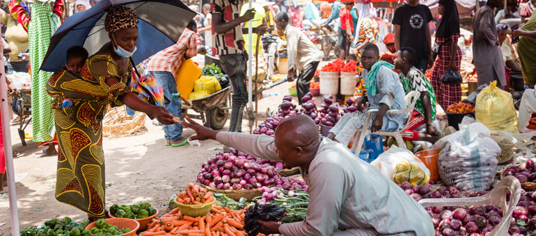 Woman with umbrella and colorful dress buying food from vendor in a market