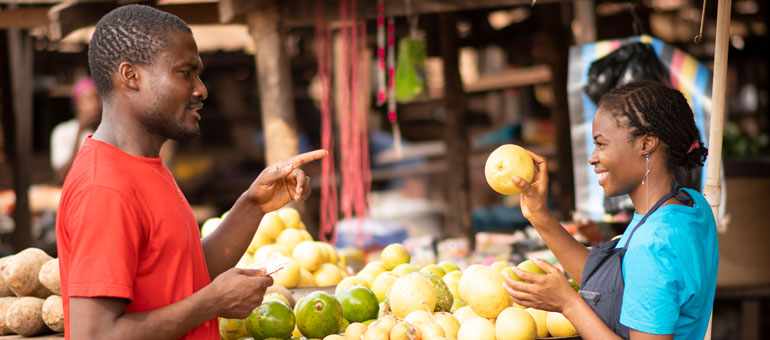 African man pointing at woman holding fruit in a market