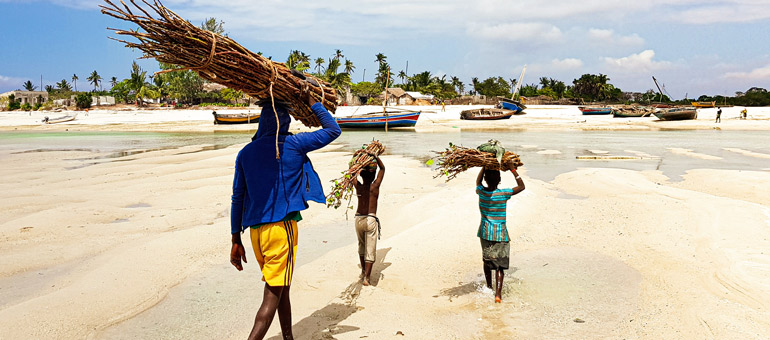 Man and two kids on the beach carrying wood on their heads