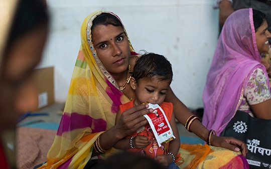 A woman in a yellow veil with her child feeding on her lap