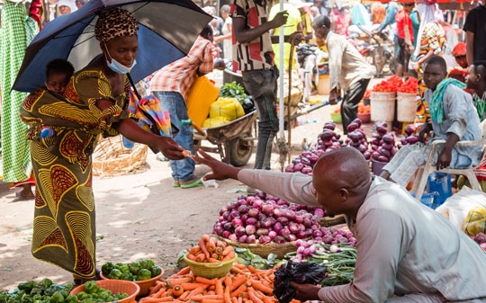 Woman with umbrella and colorful dress buying food from vendor in a market